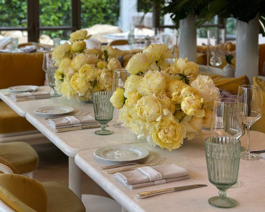 Dining table set with yellow floral arrangements, plates, and glasses in a modern restaurant setting. floral design by AY Flowers