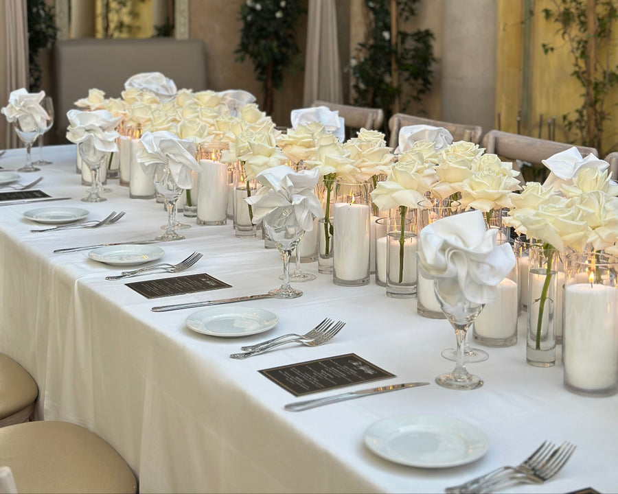 Elegant dining table setting with white flowers, candles, and silverware in a decorated room. floral design by AY Flowers