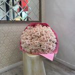 Bouquet of white roses with pink paper wrap on a wooden post indoors.