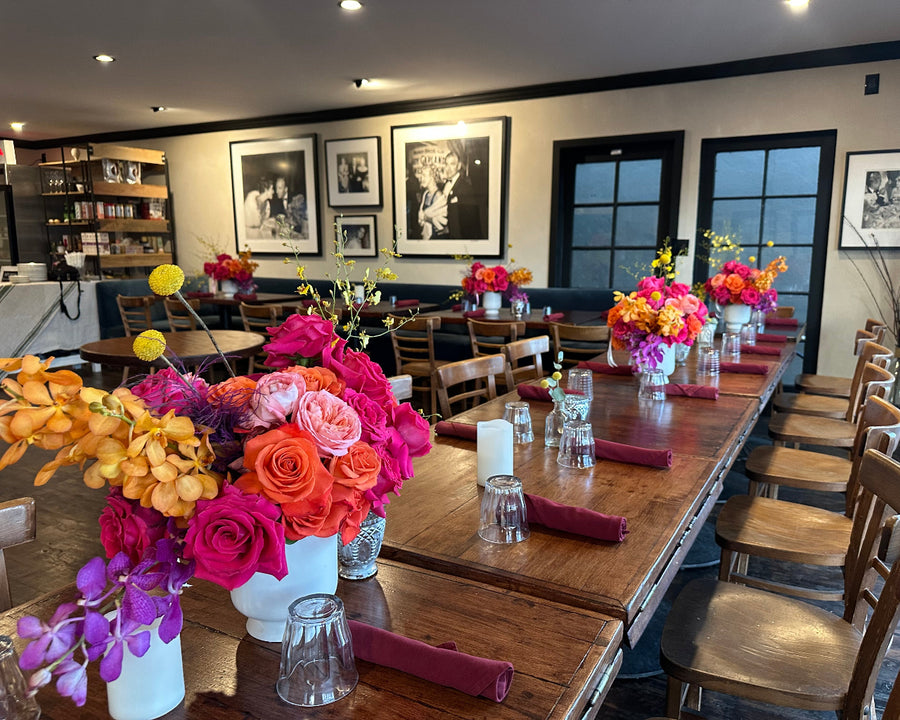 Dining room with wooden tables and chairs, floral centerpieces, and framed pictures on the wall. floral design by AY Flowers