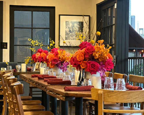 Dining room with wooden tables and chairs, colorful flower arrangements, and a painting on the wall.